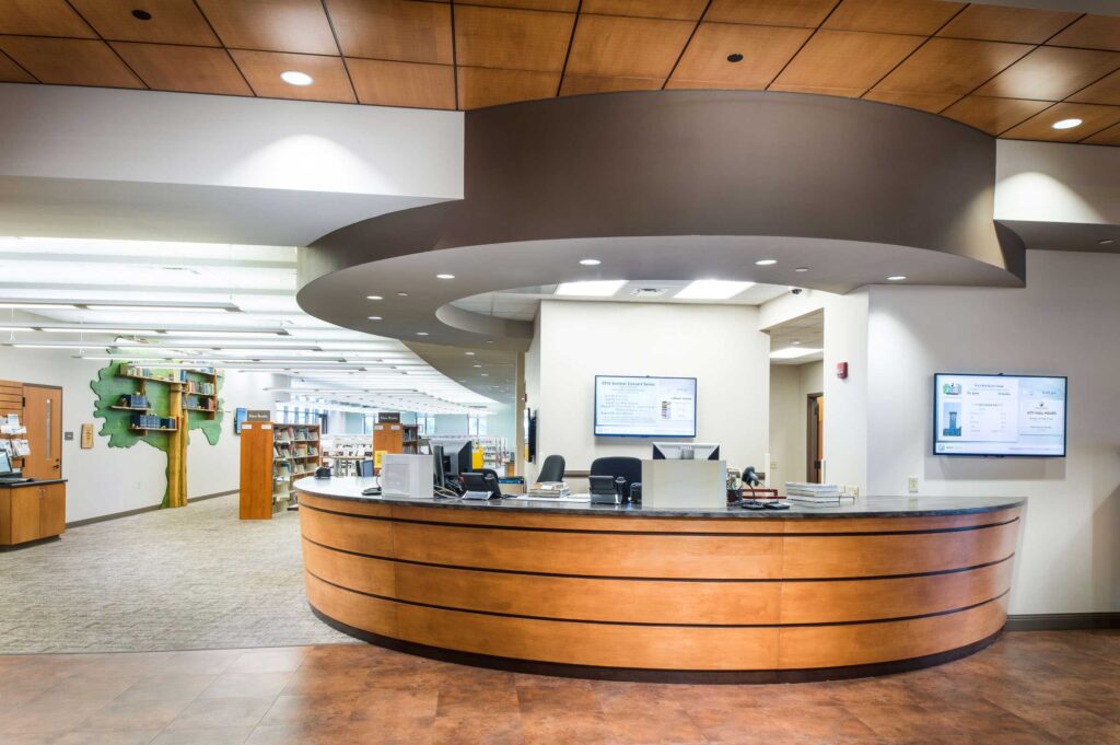 The circular front desk at Oak Creek Public Library leads into a bright media space with a tree mural