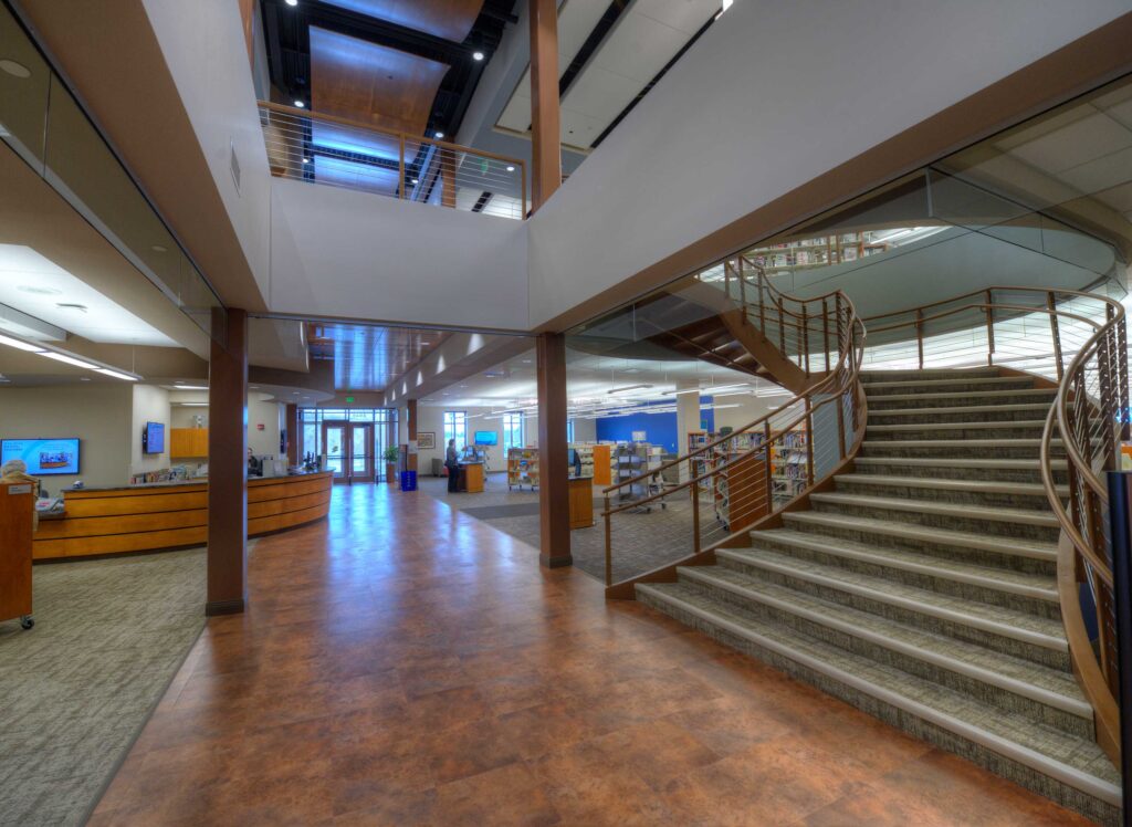 An open library space is flanked by a round information desk and a circular staircase at the Oak Creek Public LIbrary