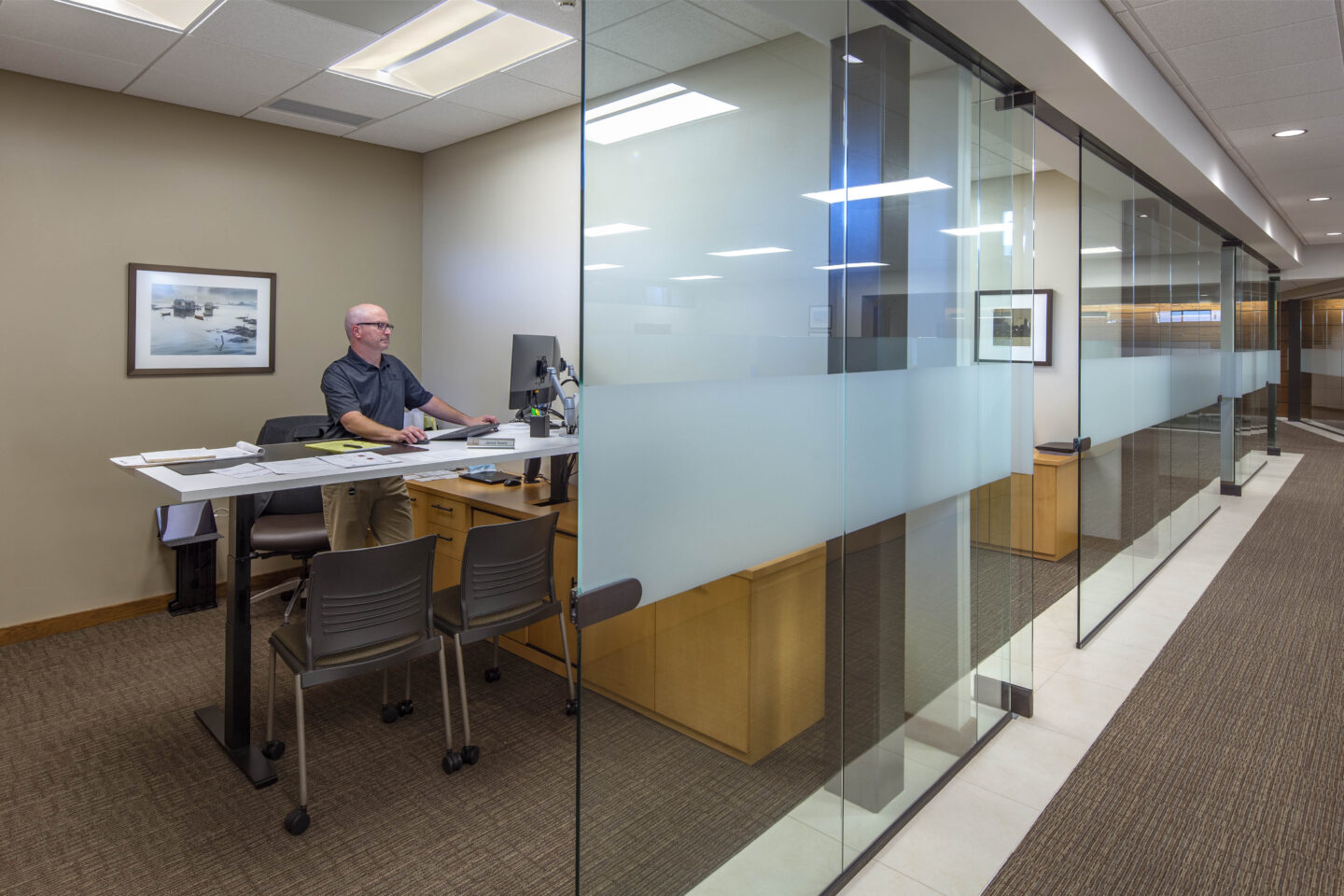 A person works from a glass-enclosed office with a view down the hallway