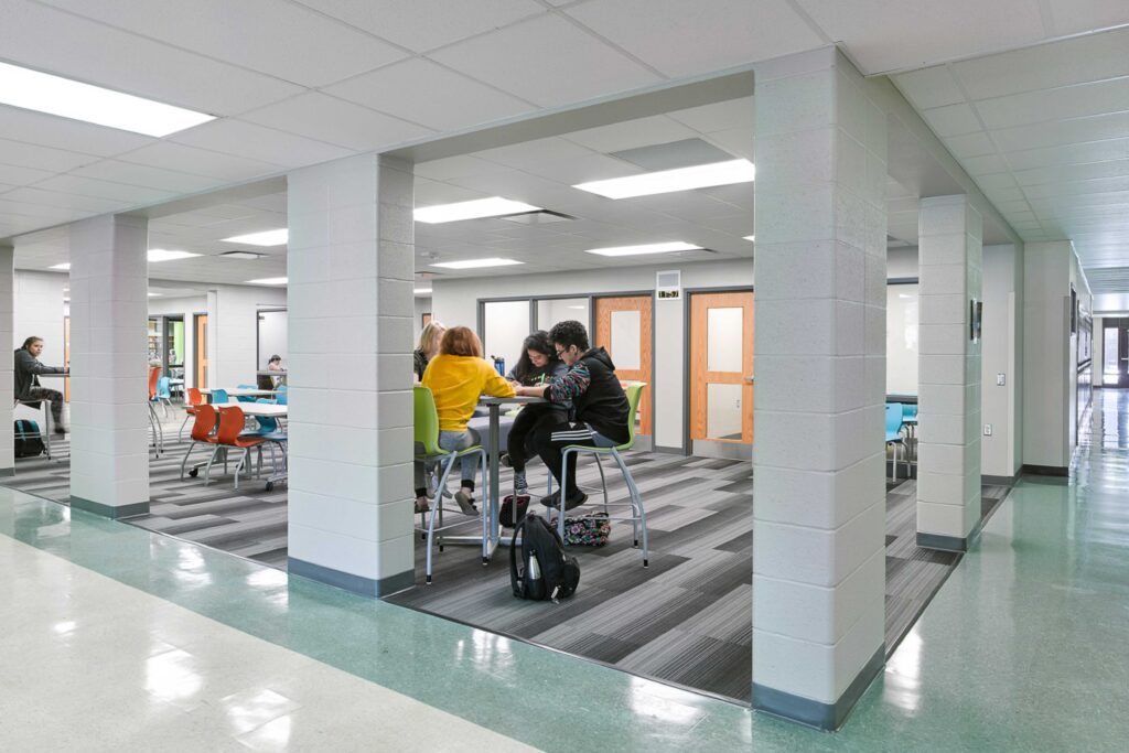 Students work together in a collaboration area with views of adjacent small group instruction rooms in the background