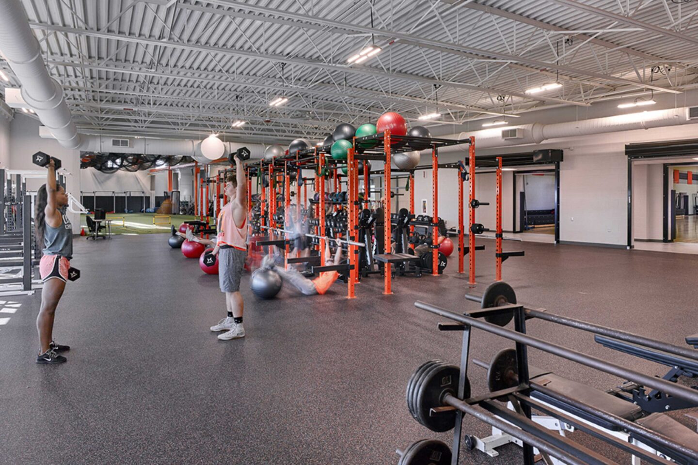 Students lift weights in the new fitness center, with glimpses into the adjacent indoor turf area and gymnasium