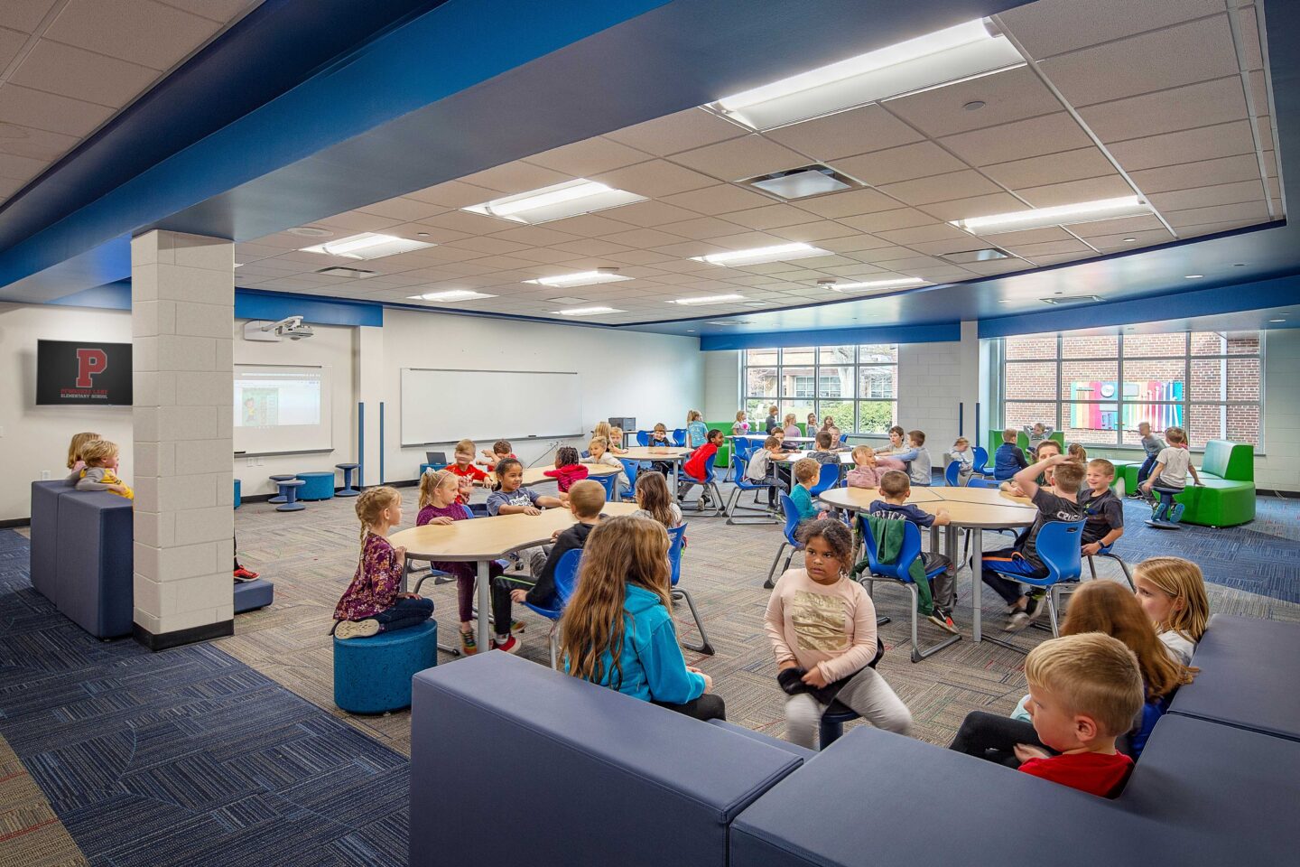 An open, windowed resource area is full of students working at a variety of furniture options at Pewaukee Lake Elementary School