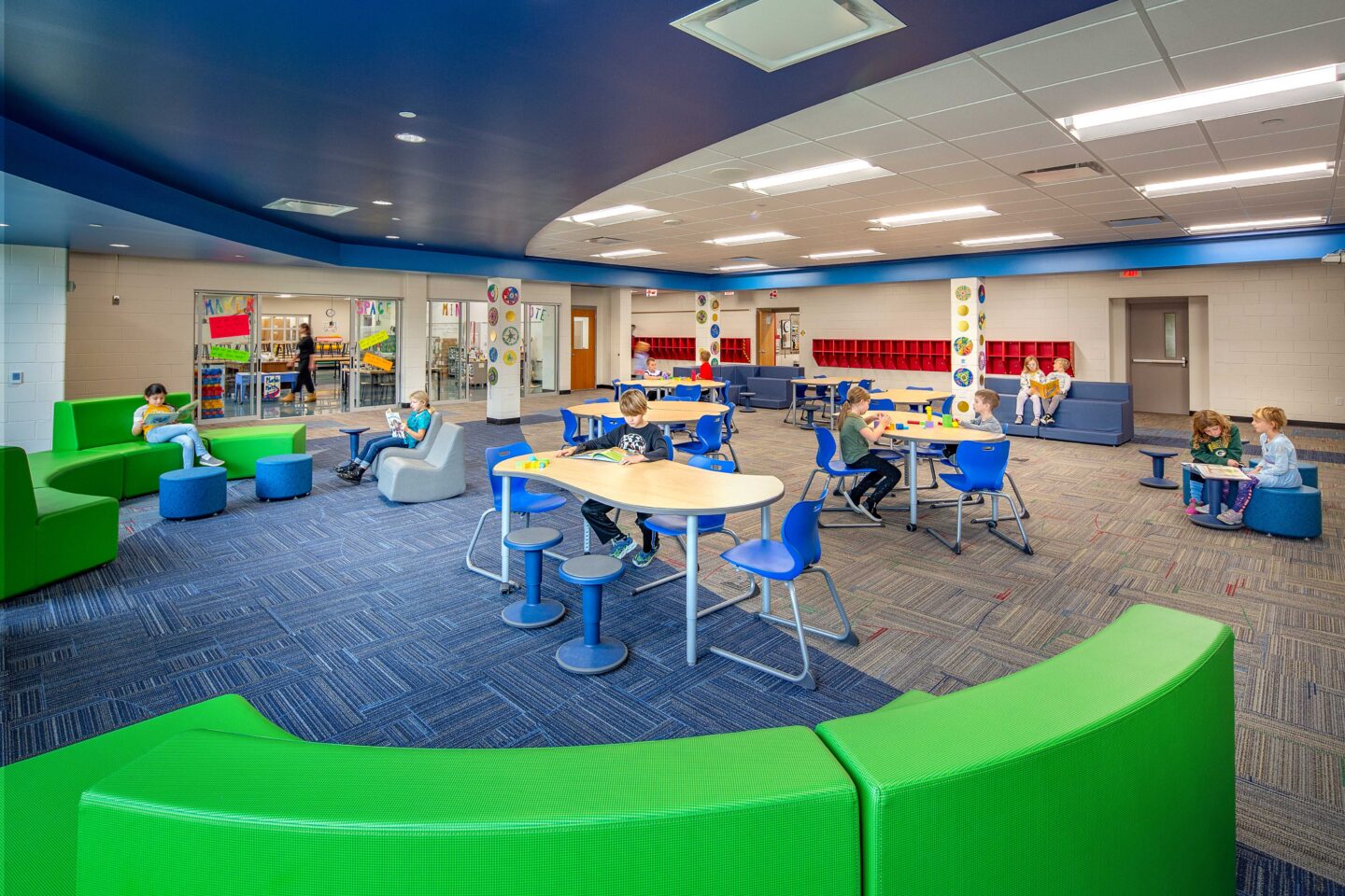 Colorful furniture lines an open resource area adjacent to a hall where students work at Pewaukee Lake Elementary School