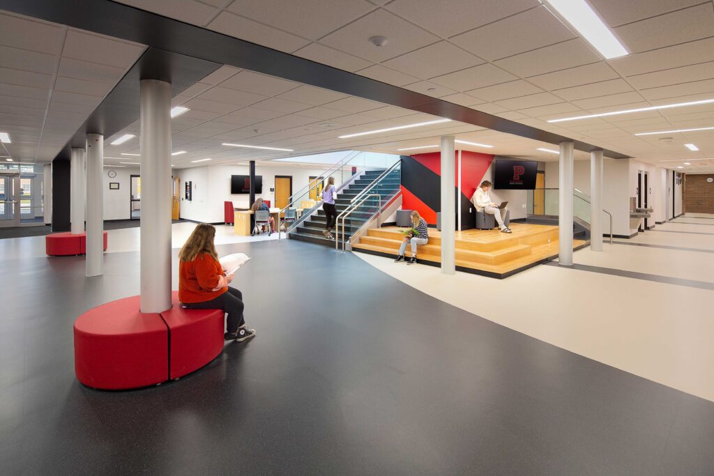 Furniture and stairs offer seating for students in an open area below a wide learning staircase at Pewaukee High School