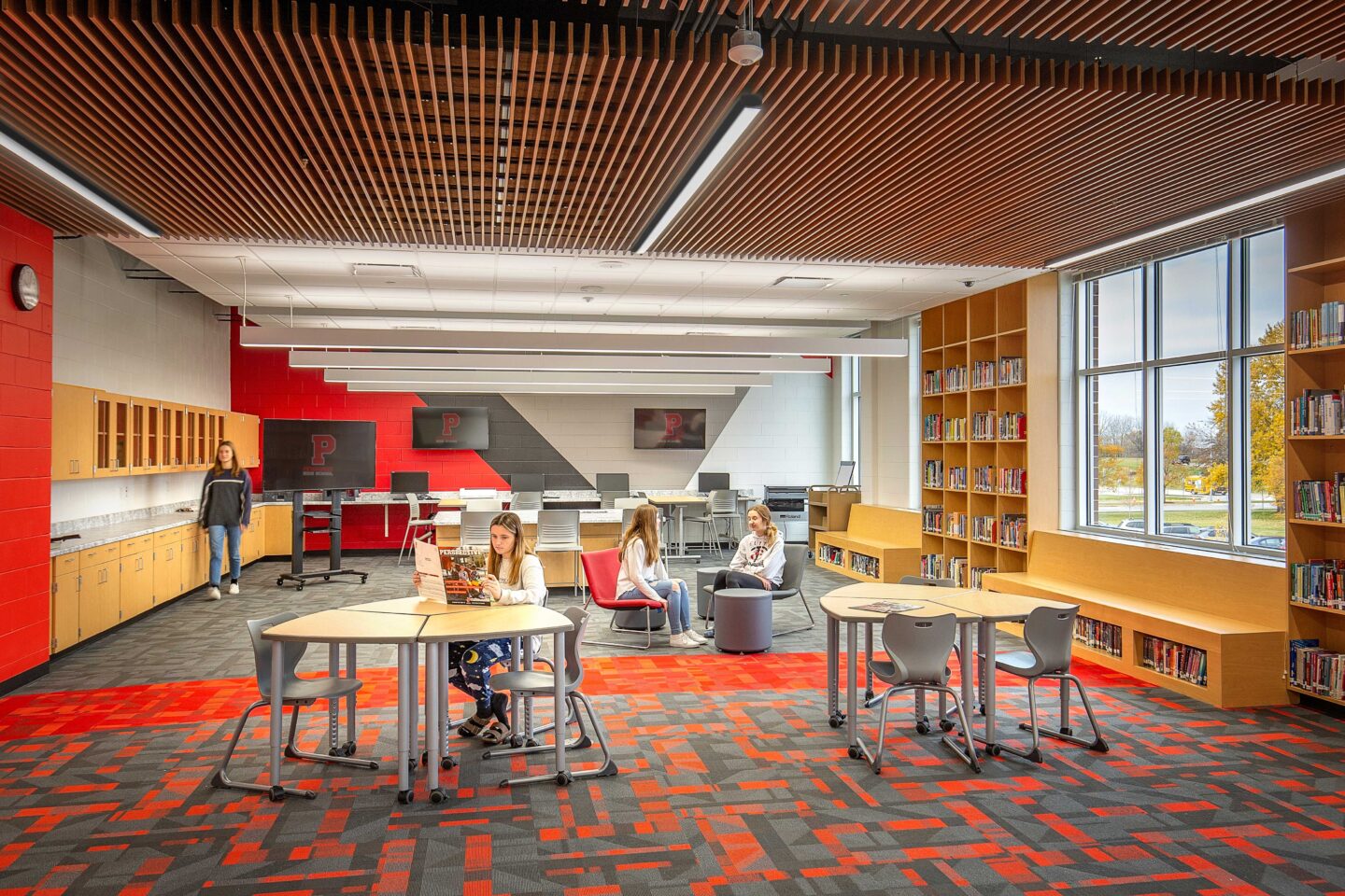 A colorful, comfortable, and windowed library gives students space to work and study, with colorful accents in school colors at Pewaukee High School