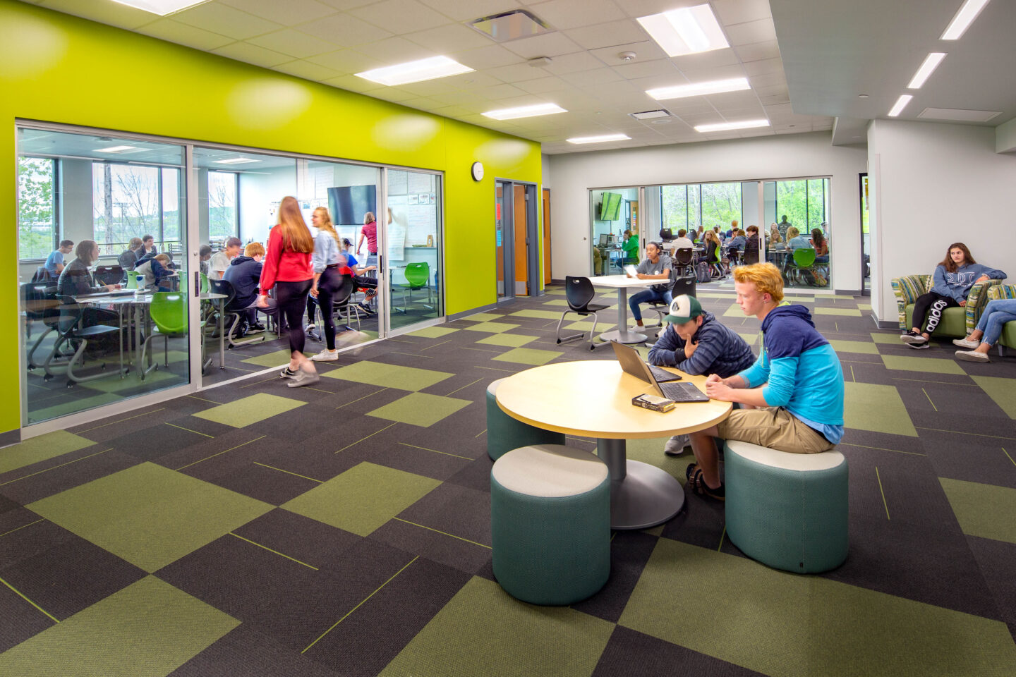 Port Washington high school students conversing in the collaboration area with furniture and glass sliding doors to a classroom