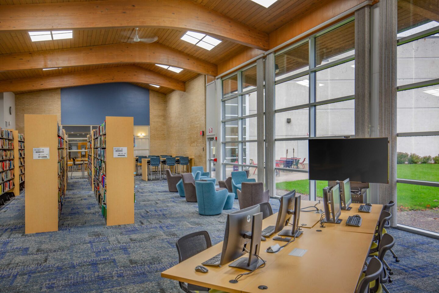 A curved wooden ceiling connects an open library space to a large wall of windows