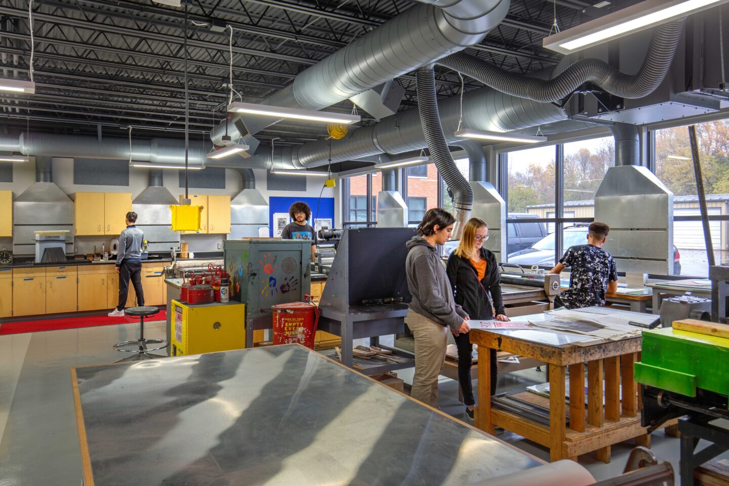 Printmaking students work in a room filled with equipment and lined with windows