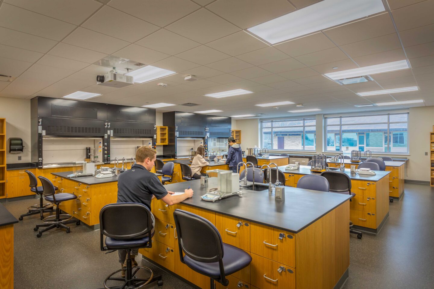 Students work at a cluster of lab tables with windows in the background