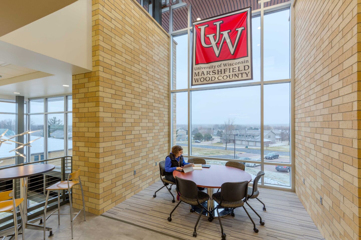 A student studies at a round table in a windowed alcove with a university banner above
