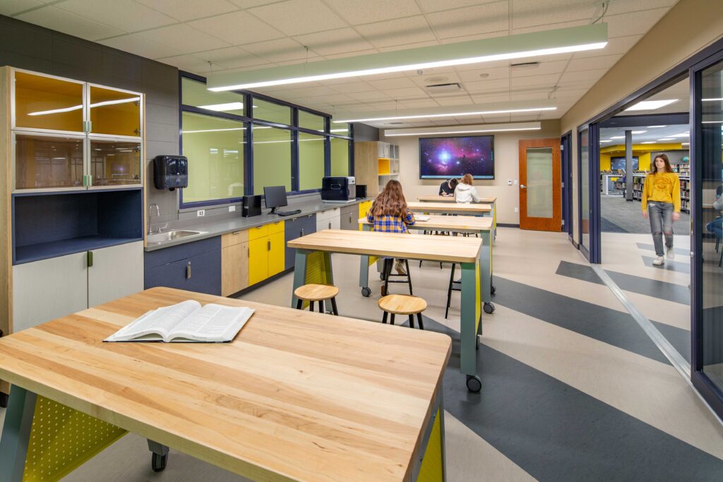 Students sit at high tables in an Innovation Center for STEAM off of a larger library space