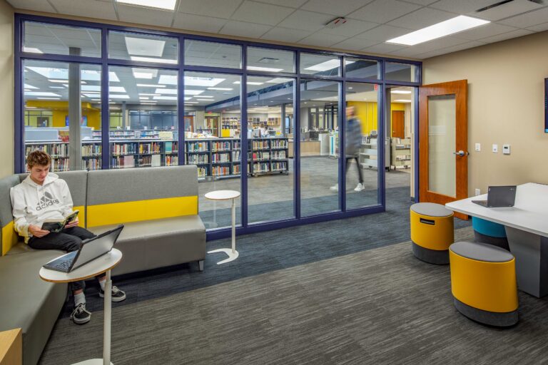 A space for larger groups looks out onto a bright library area through a glass wall