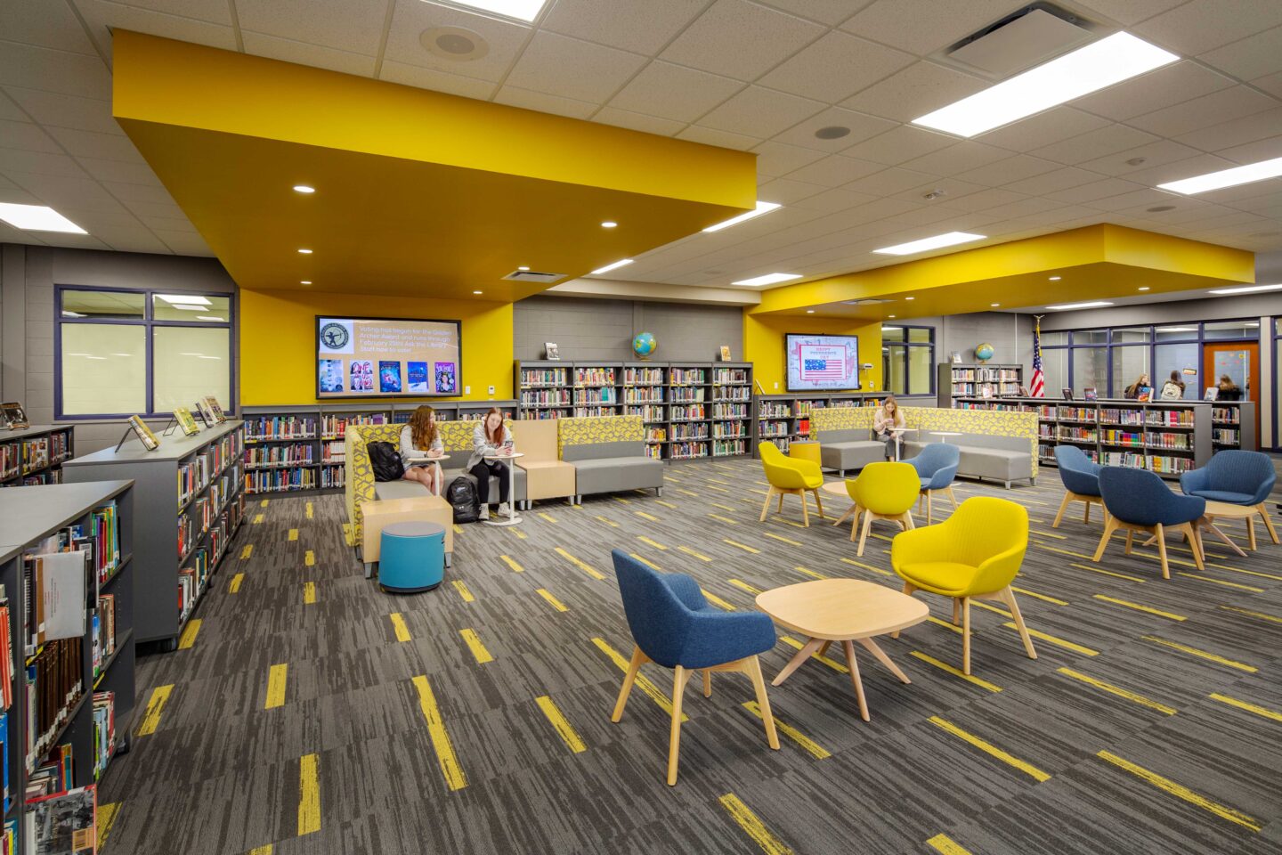 A library space comes to life with brightly colored, modern furniture and yellow call-out features in the ceiling