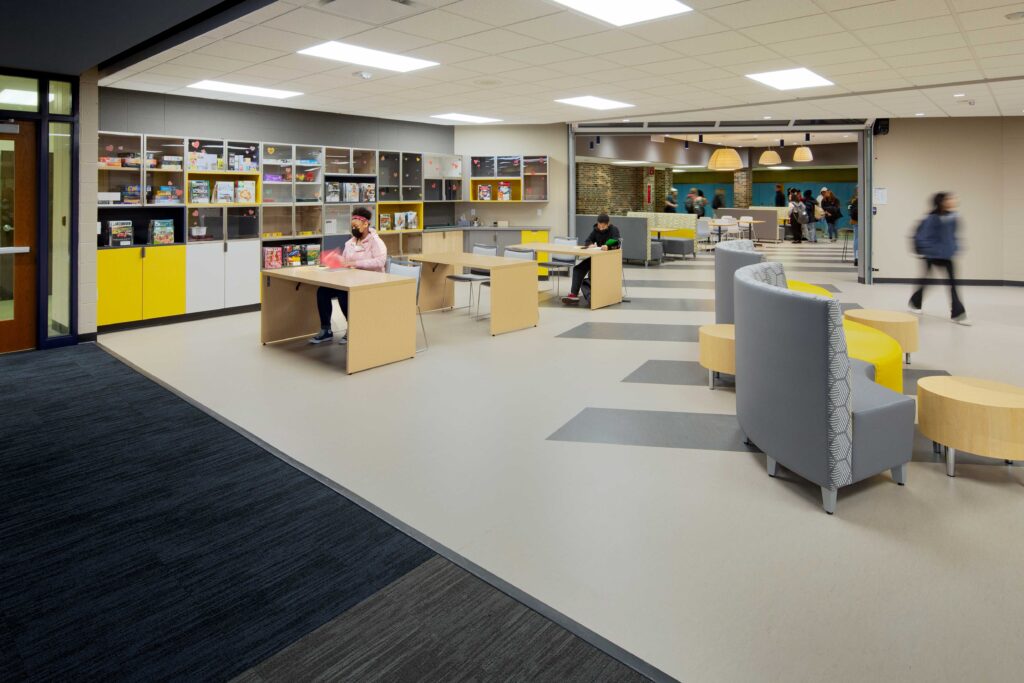 A study area with flexible furniture leads from the library to the cafe area beyond