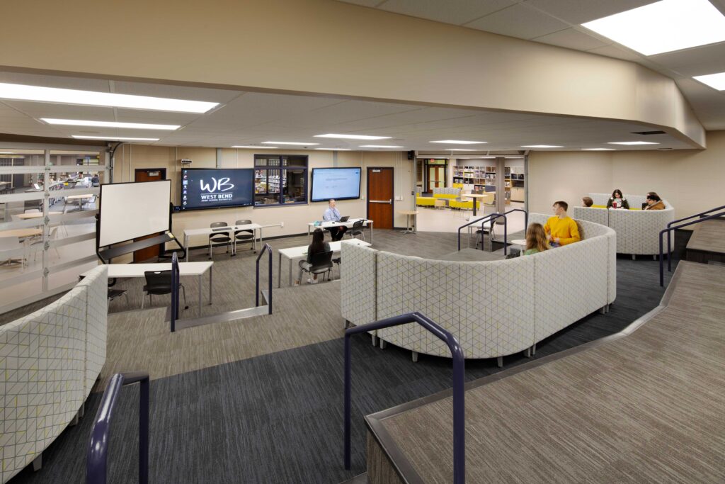 A teacher instructs students in a flexible auditorium-style classroom connected to the larger library by open garage-door entrances