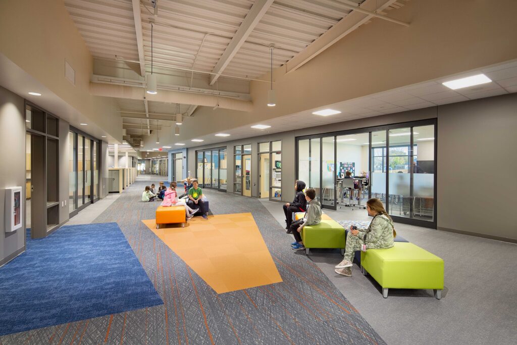 The collaboration areas feature colorful furniture and flooring details with classrooms accessible nearby via large sliding glass doors