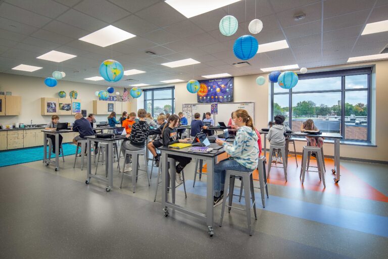 Students work at tables in a science classroom with large windows.