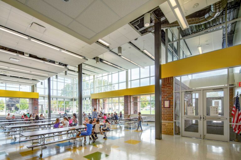 A high-ceilinged cafeteria with walls of windows features color accents and a separate entrance at Knapp Elementary in Racine