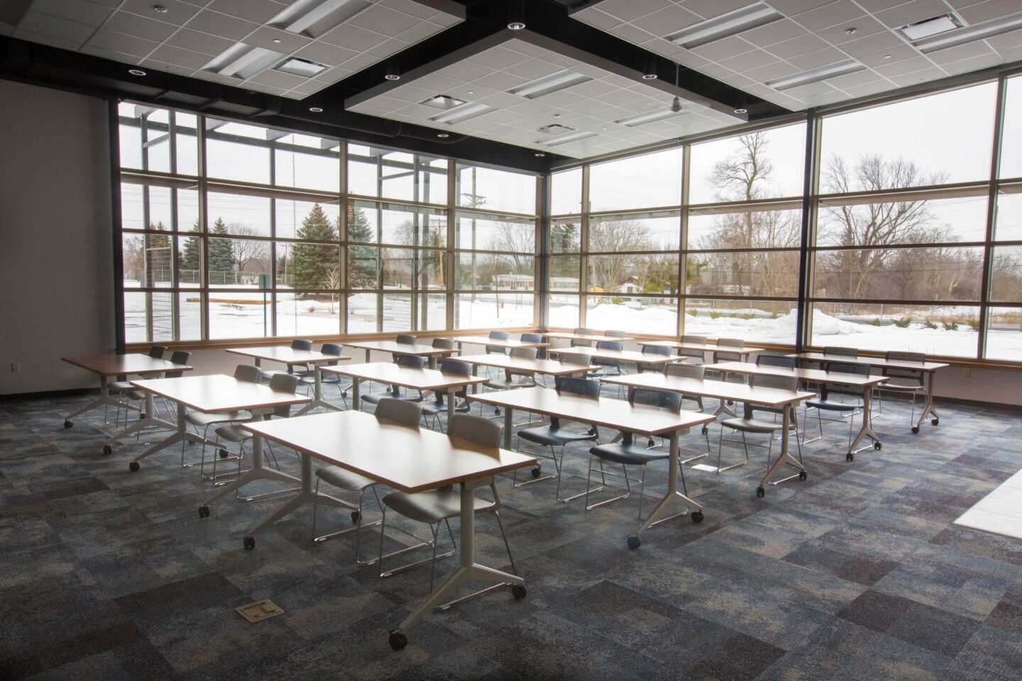 View from front corner of an open training room with tables and chairs, lined with two window walls