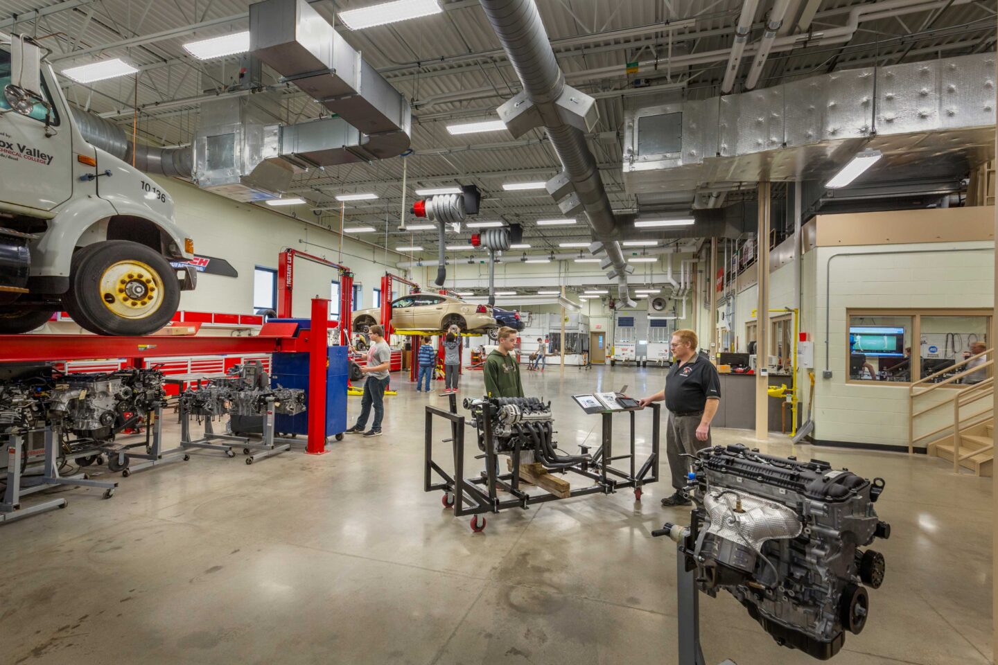 Students and teachers work in a large, active auto shop adjacent to a classroom space at Wausau East High School