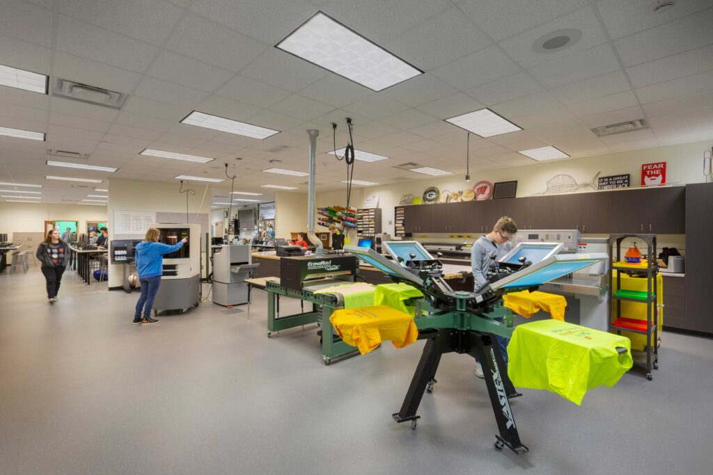 Students screenprint T-shirts in the foreground of an expansive tech and graphics space at Wausau East High School