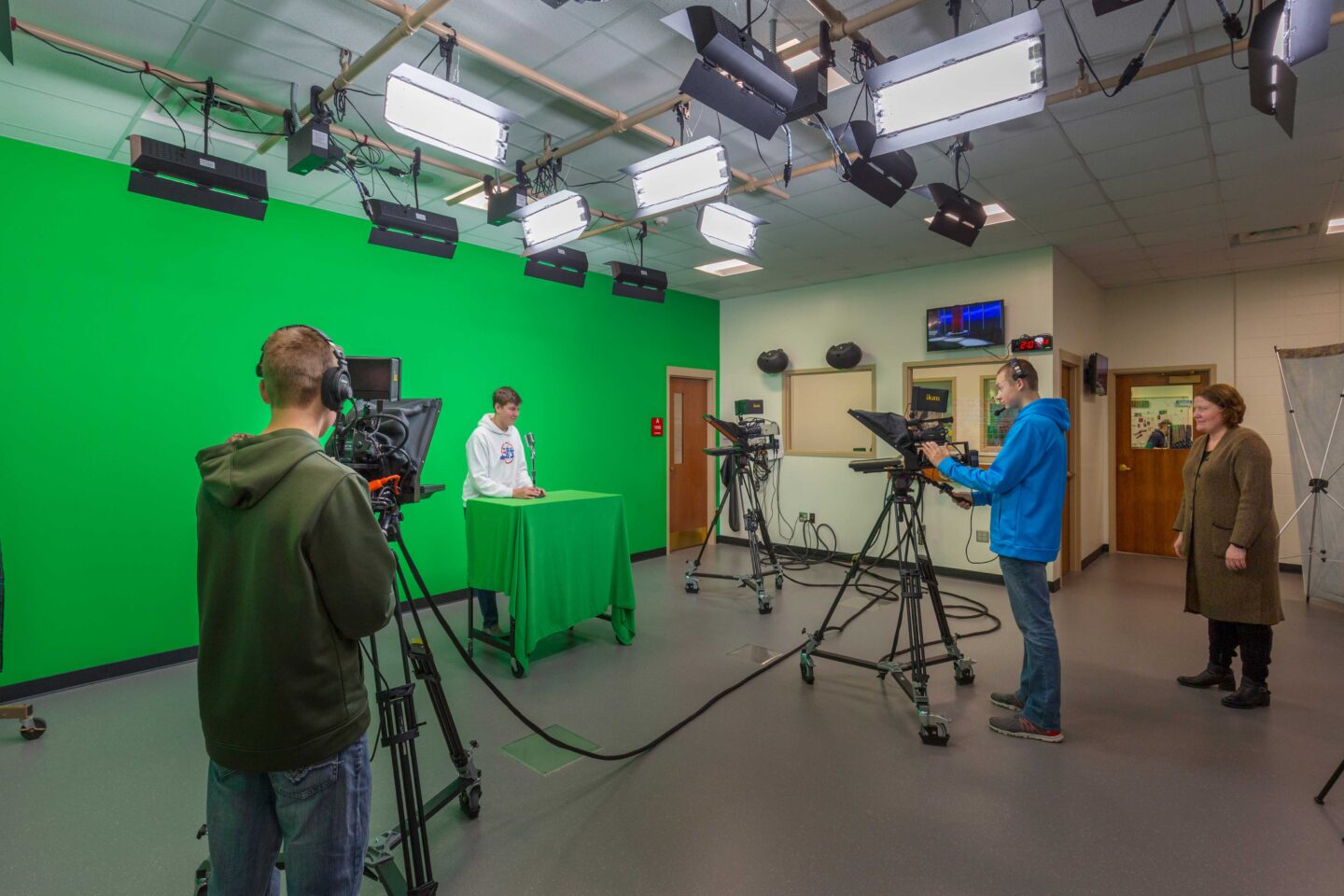 Students work behind and in front of cameras at a broadcast studio with a large green screen, located at Wausau East High School