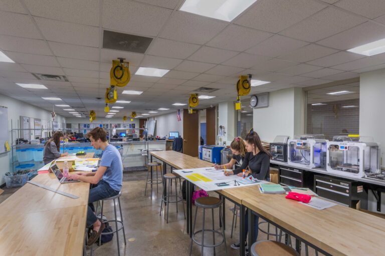 Students work at long, open tables that lead into a computer lab, with STEM equipment available at Wausau West High School