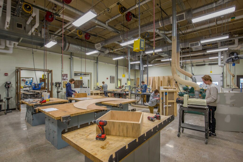 Students work at tables and equipment for woodworking inside a large, industrial woods shop at Wausau West High School