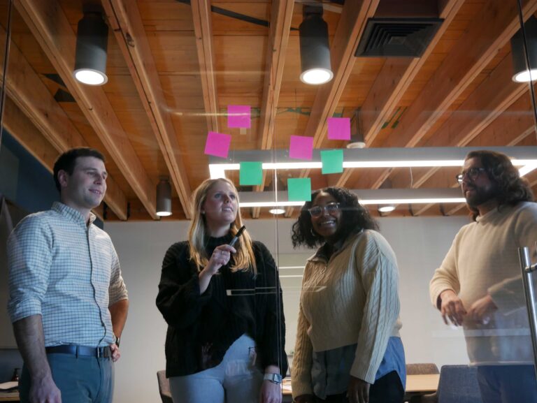 Four Bray team members gather around a glass panel with sticky notes