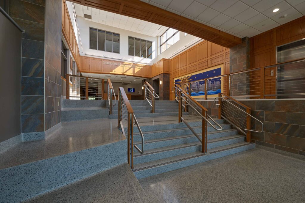 A view of the terrazzo stair leading to a bright, naturally-lit atrium surrounded by elegant wooden wall panels
