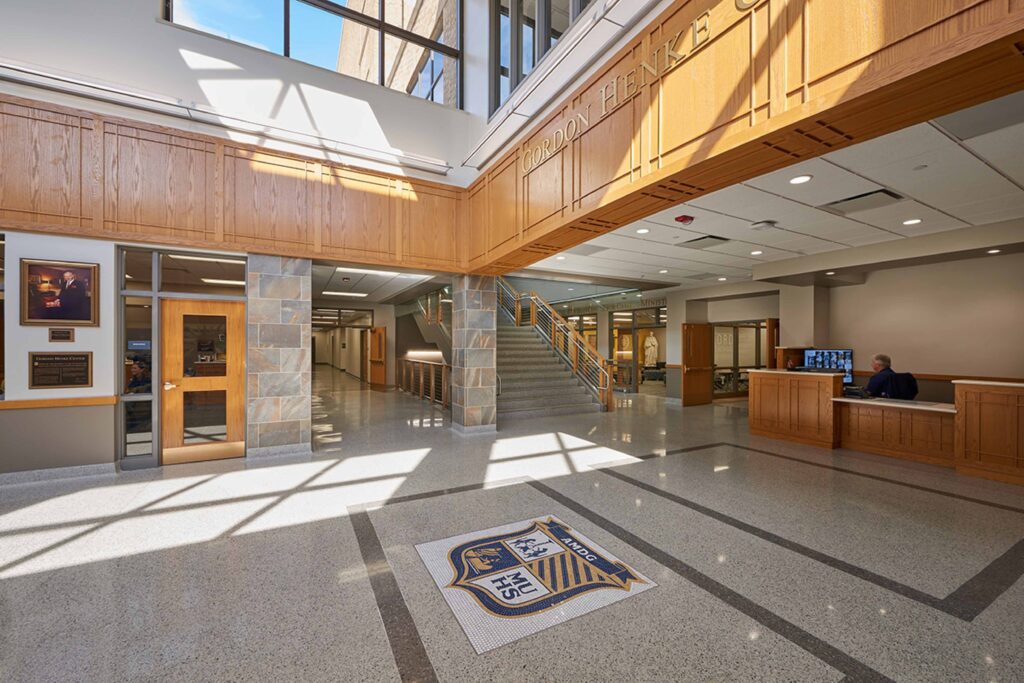 A view of the brightly-lit lobby featuring tall clerestory windows and a tile mosaic of the school emblem on the floor