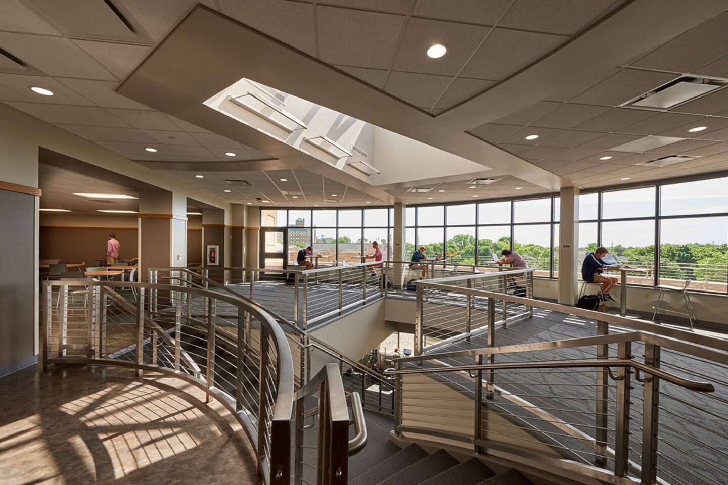 Students work in front of large windows on the second level of the lounge