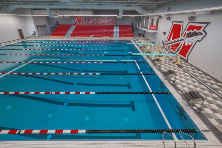 An elevated view of the pool looking towards the starting blocks, diving boards, and bleacher seating