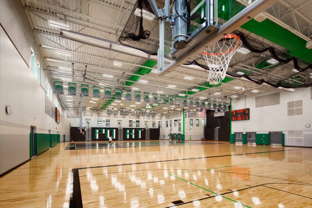 An overall view of the gymnasium looking towards the bleachers and windows that connect to the upper cafeteria
