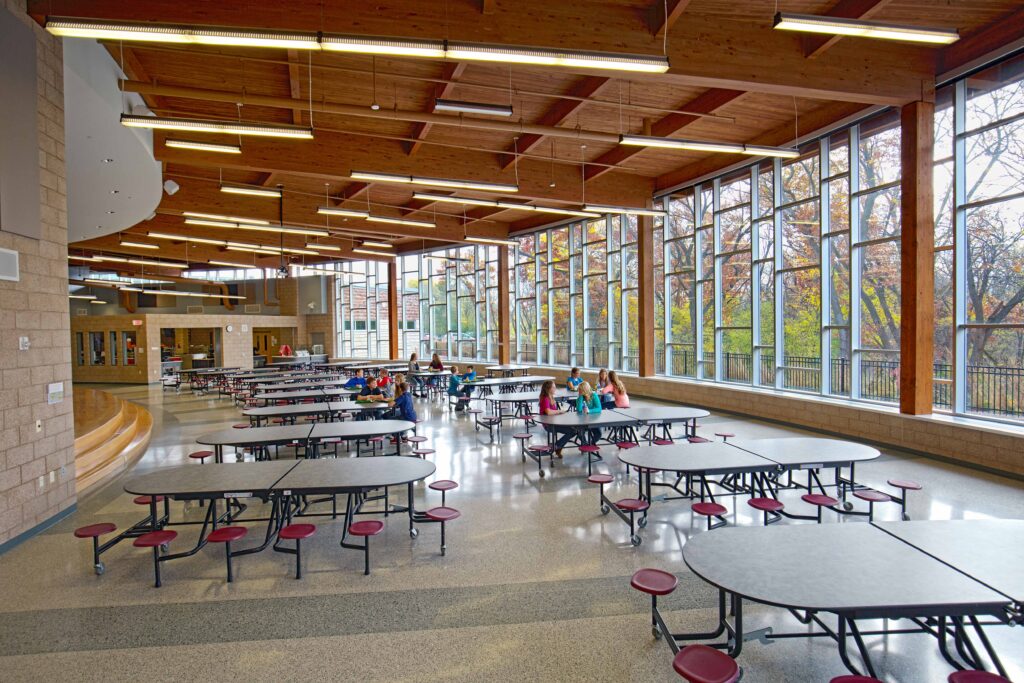 A view of the school's cafeteria featuring large windows and stage for performances and speakers