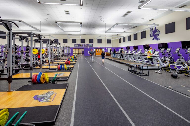 Beloit Memorial High School fitness center featuring squat racks, cardio machines and a short 3-lane track