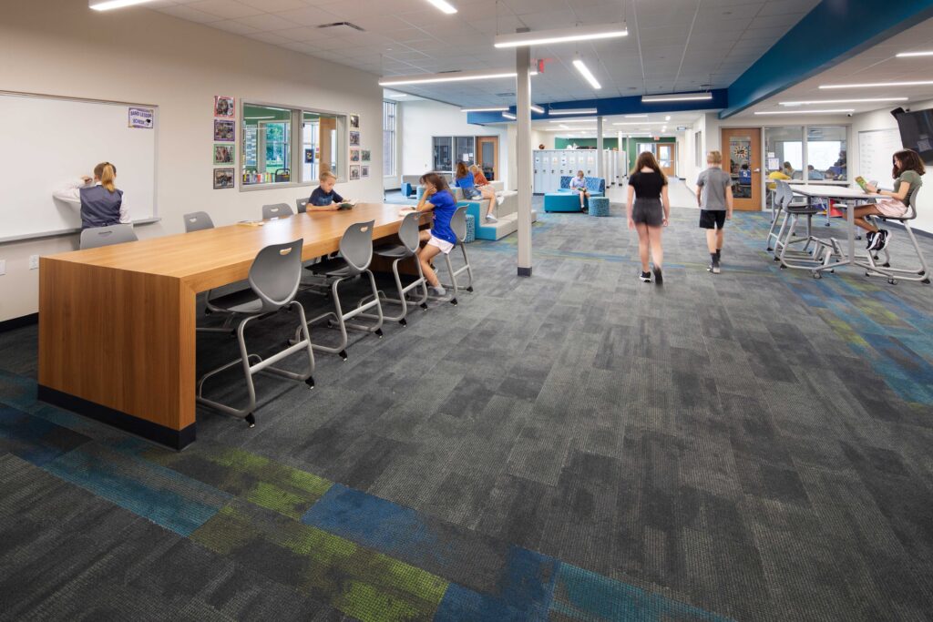 JC McKenna Middle School Resource Area looking west with students walking in the hallway and sitting at the tables