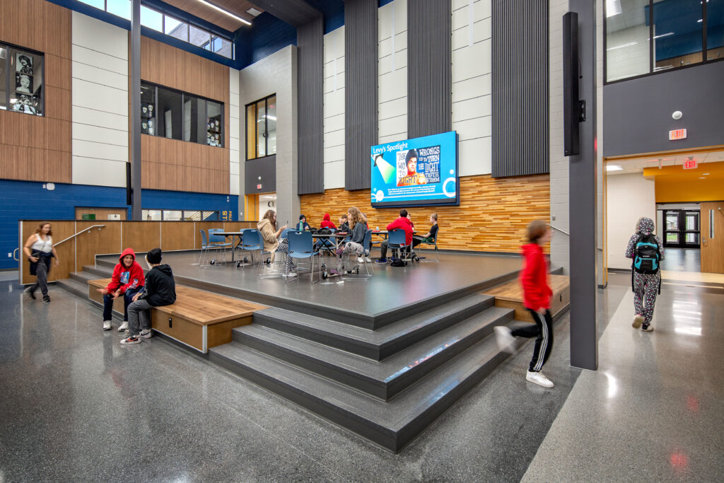 Commons/Cafeteria stage with monitors and students eating lunch at Vel Phillips Middle School