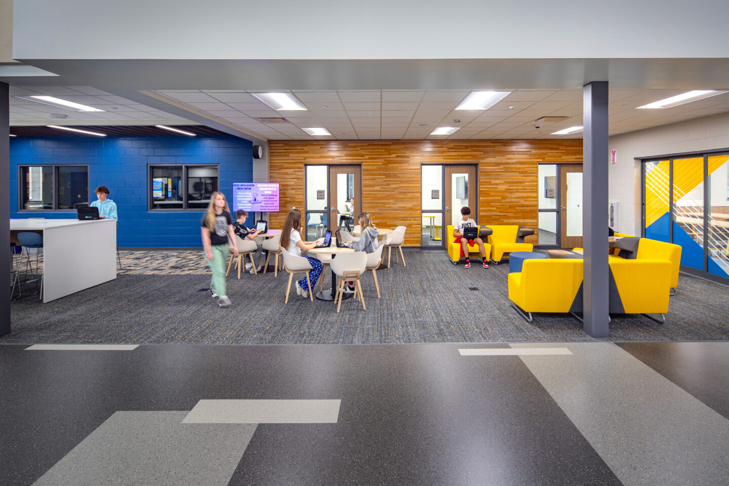 Production studio at Vel Phillips Middle School with reclaimed wood wall and glass sliding doors on the right side of the photo with branding that opens to the makerspace room. On the left side of the photo is an island to work/study at.