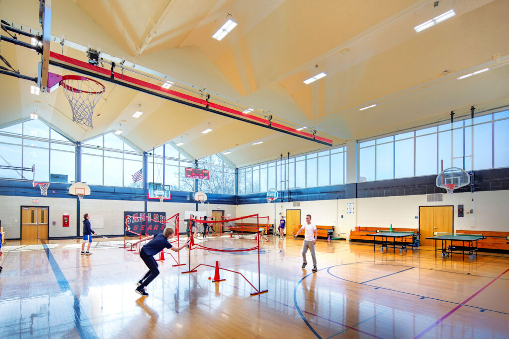 Gymnasium with students playing activities at Sabish Middle School. Large amount of windows to allow natural light in.