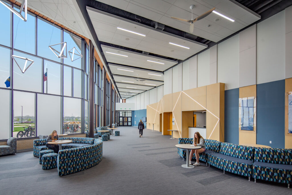 Performing Arts Center lobby with flexible furniture and ticket booth. Hanging triangular lights are in front of the floor-to-ceiling windows.