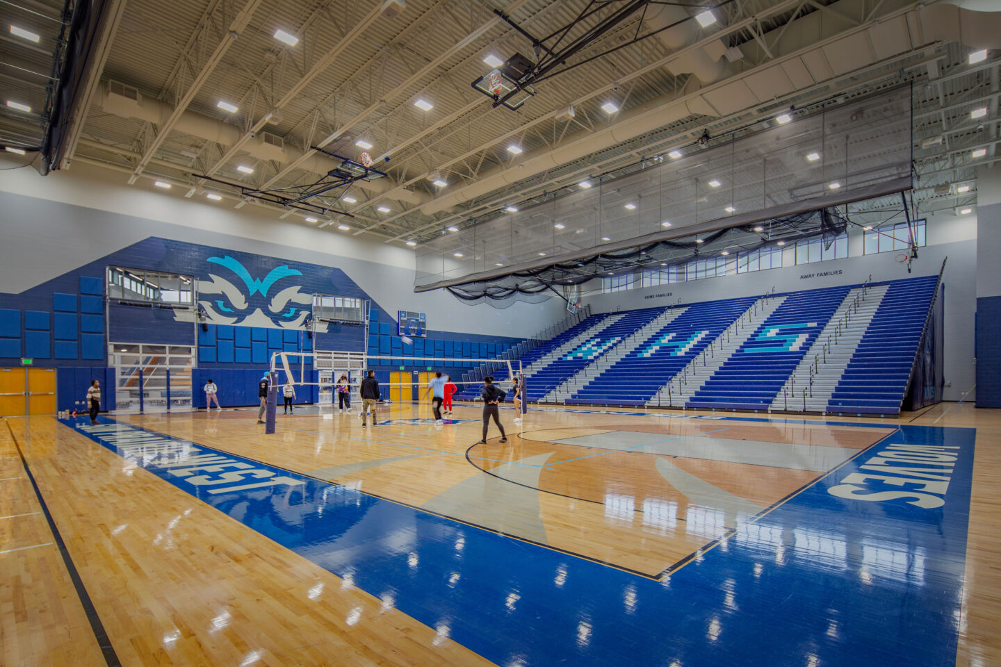 Main gym court with branded bleachers pulled out and garage doors looking into the commons/cafeteria area