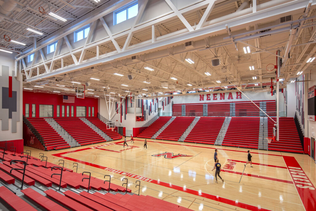 Competition gym with three sides of bleachers down and students playing on the basketball court