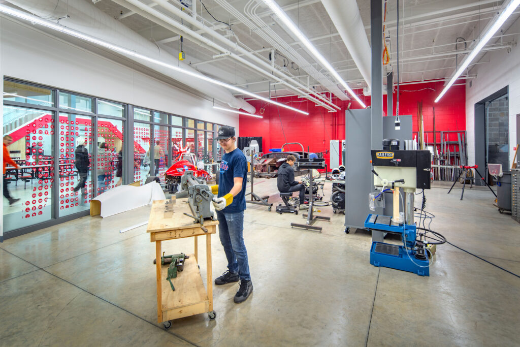 Manufacturing lab with two students working on machines and clear windows to the cafeteria for visibility into the program